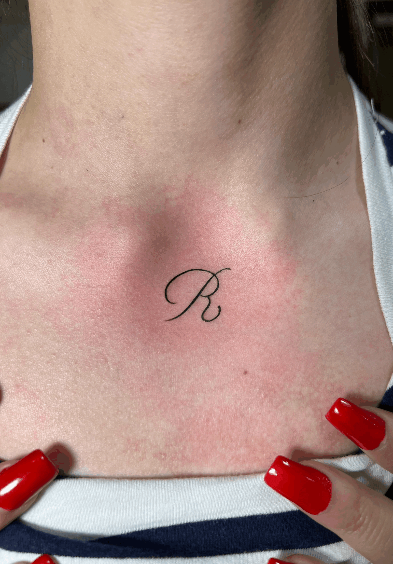 Tatuaje minimalista de letra R en pecho estilo fine line delicado