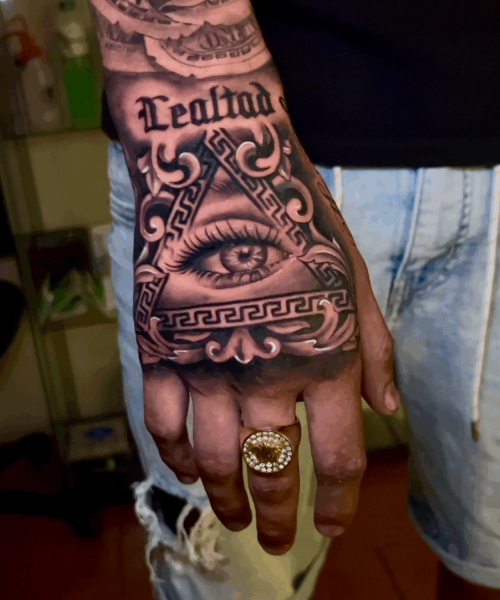 Tatuaje en mano con ojo, texto Realidad y elementos decorativos chicanos en estilo realista