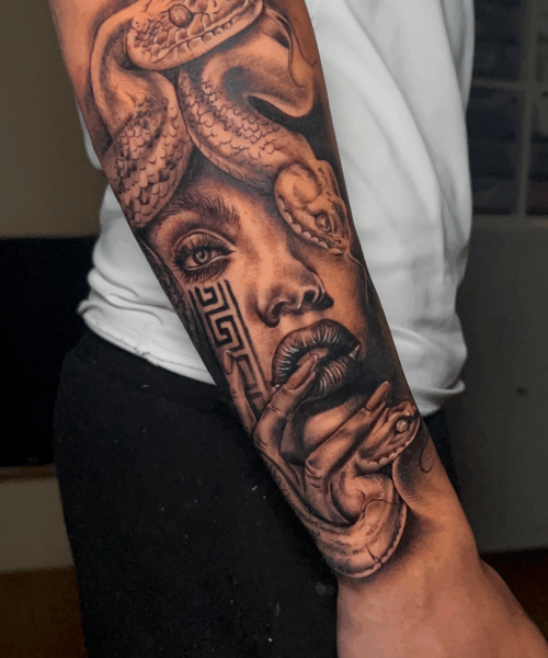 Tatuaje en brazo de rostro femenino con serpiente y elementos decorativos aztecas en estilo realista